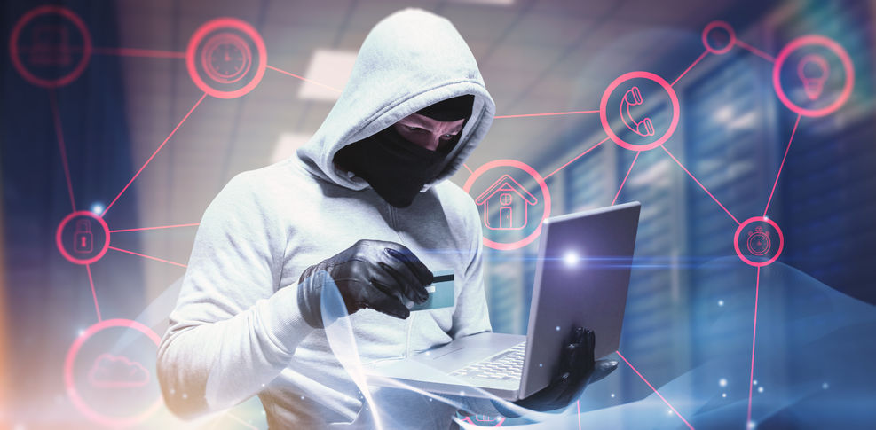 Man wearing a white hooded sweatshirt and a mask holding a credit card and laptop